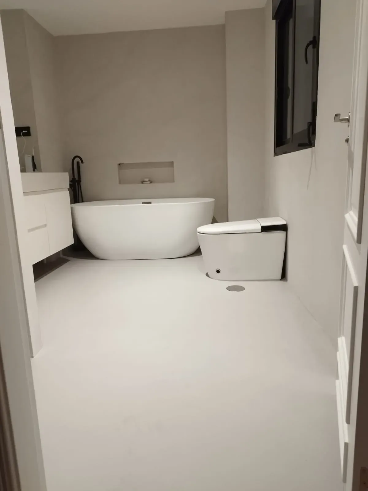Baño con grifería blanca: bañera, inodoro y lavabo. Paredes claras y ventana.