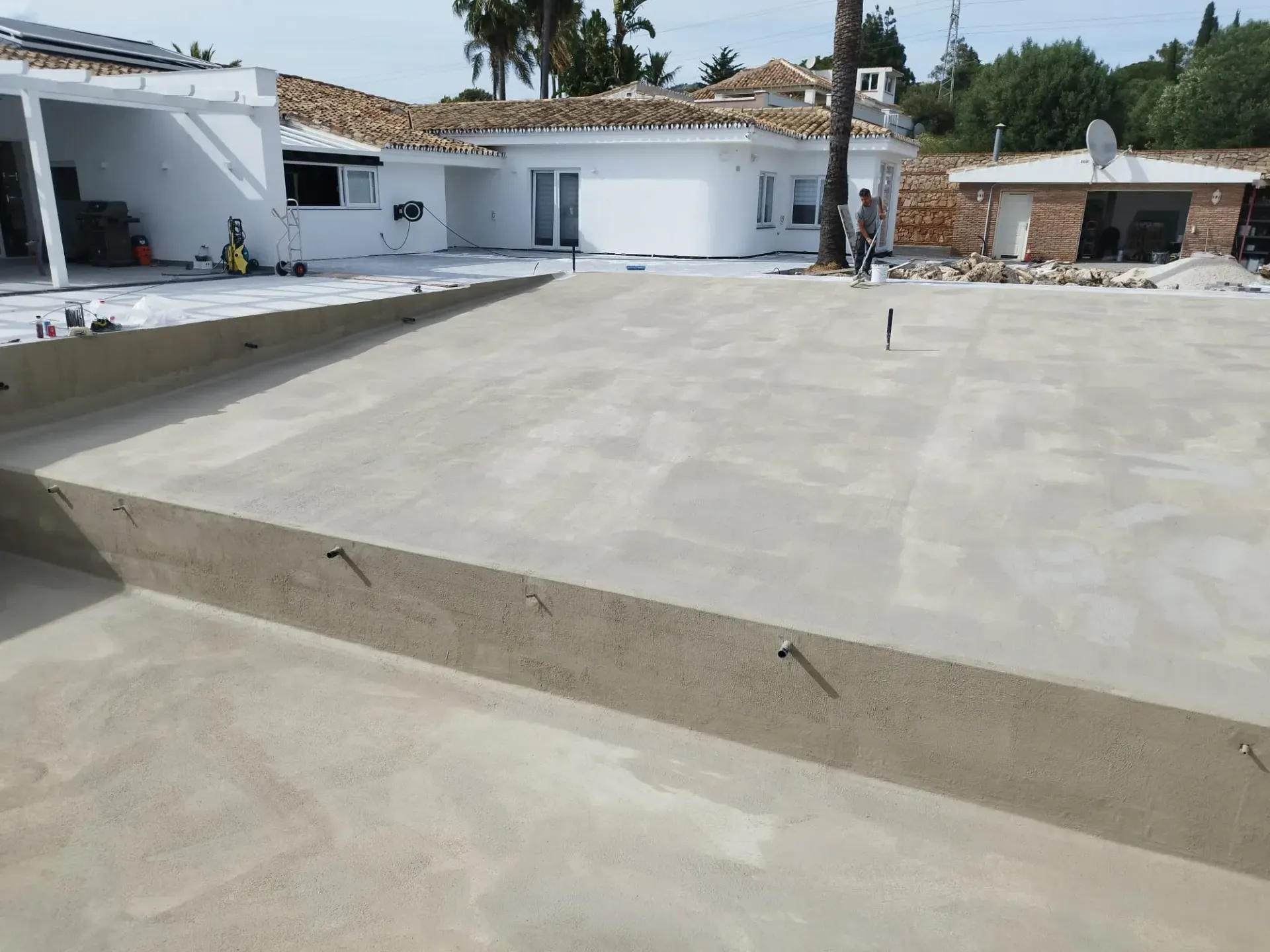 Piscina de hormigón de nueva construcción, parcialmente llena, rodeada de un edificio blanco en un entorno exterior soleado.