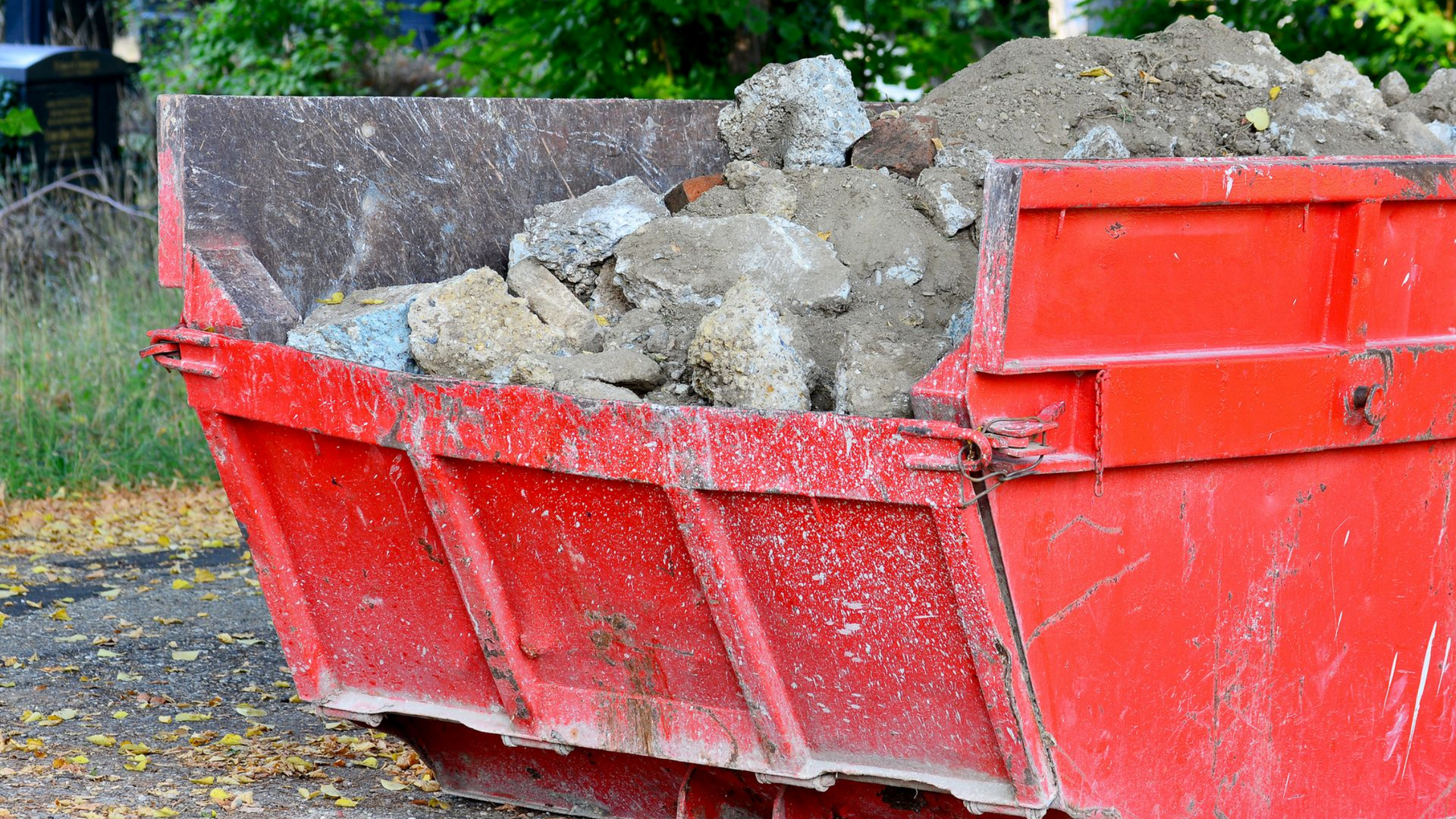 Benne rouge remplie de débris de construction, à l'extérieur.