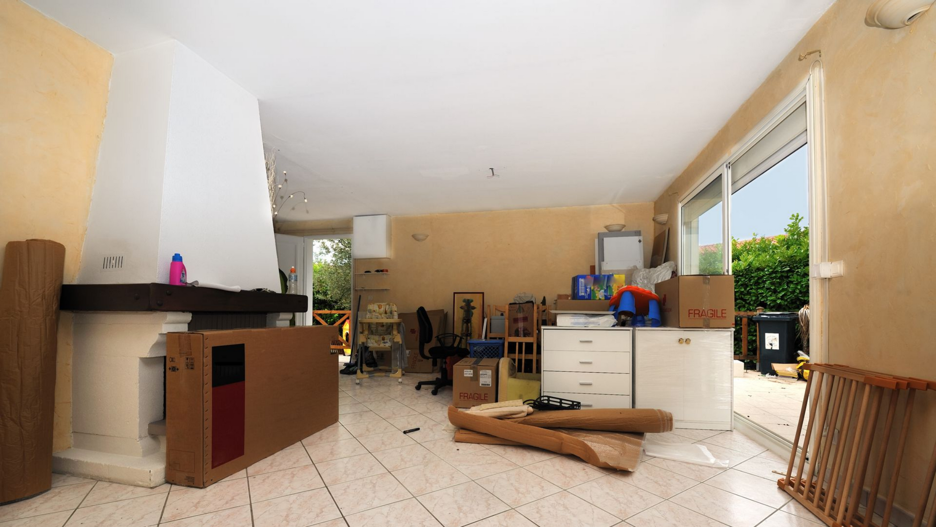 Salon vide avec cheminée, sol carrelé blanc, caissons et porte coulissante en verre.