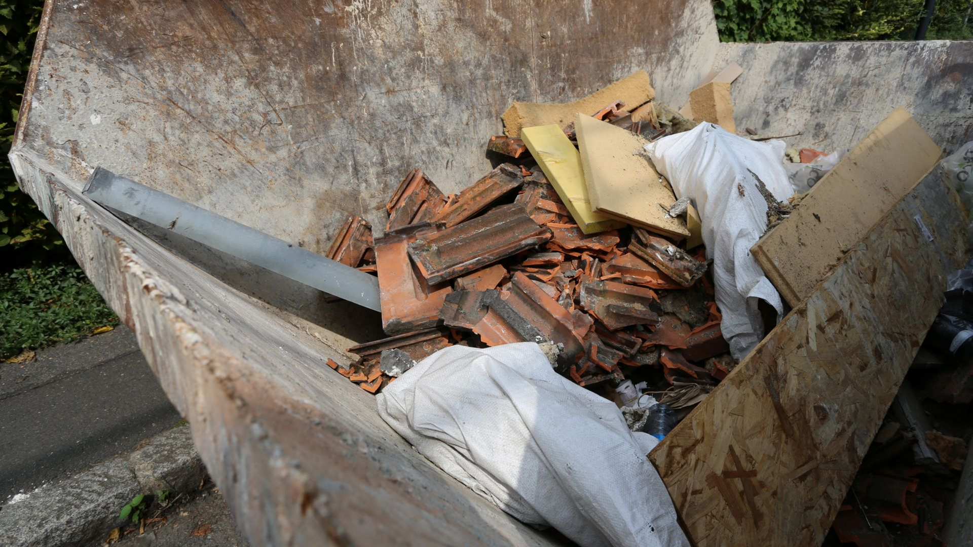 Conteneur rempli de débris de construction, y compris des tuiles cassées et du bois.