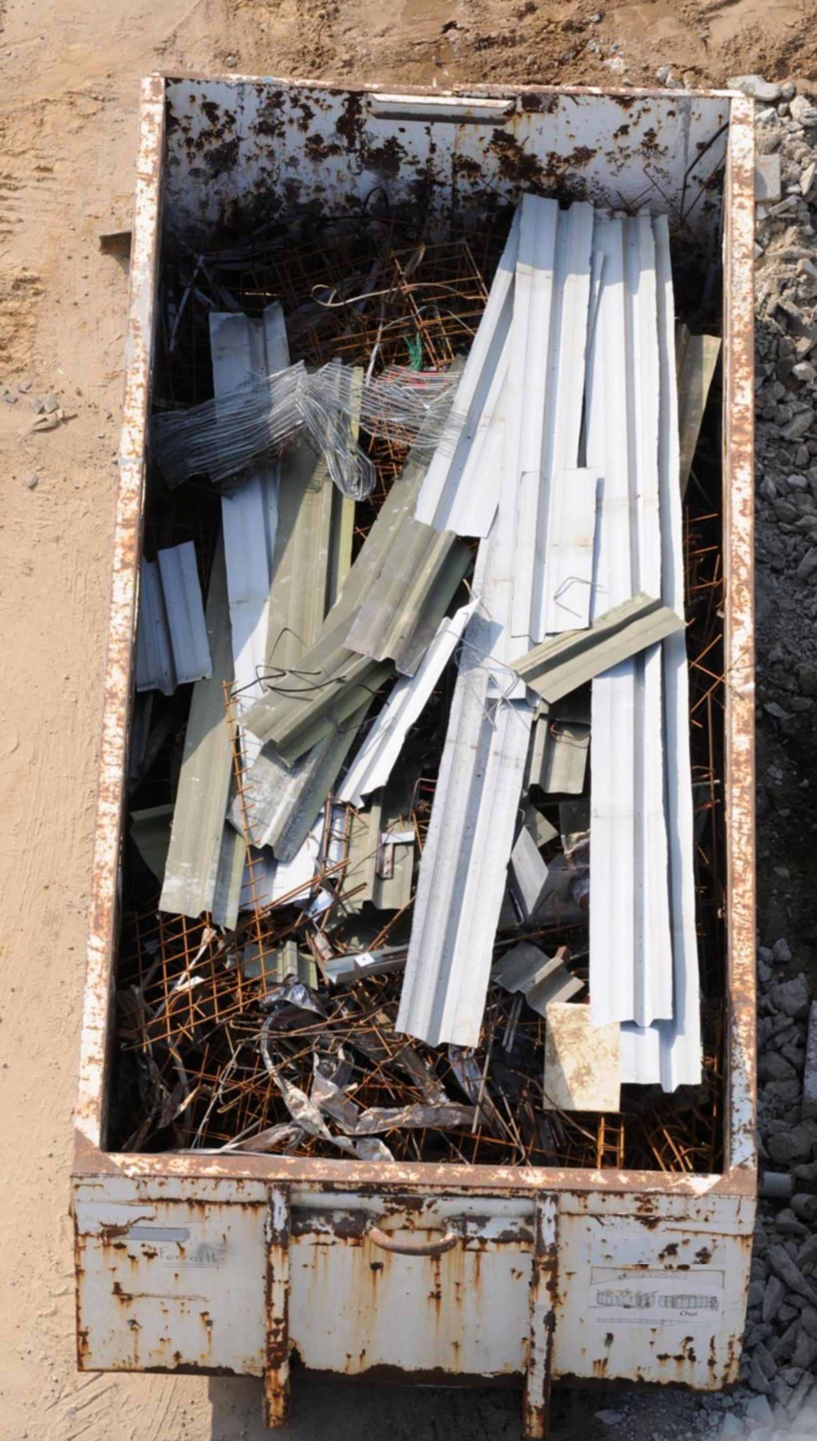 Conteneur en métal rouillé rempli de ferraille et de matériaux de toiture ondulés.