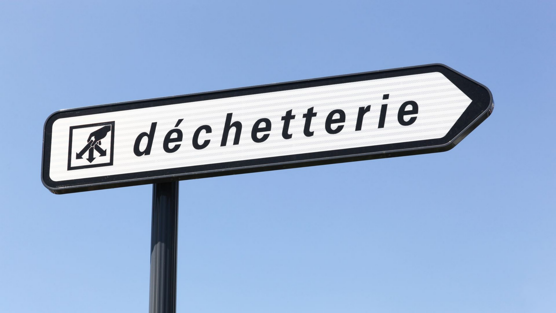 Panneau indiquant la direction à droite, indiquant « déchetterie » avec un symbole de recyclage, sur fond de ciel bleu.