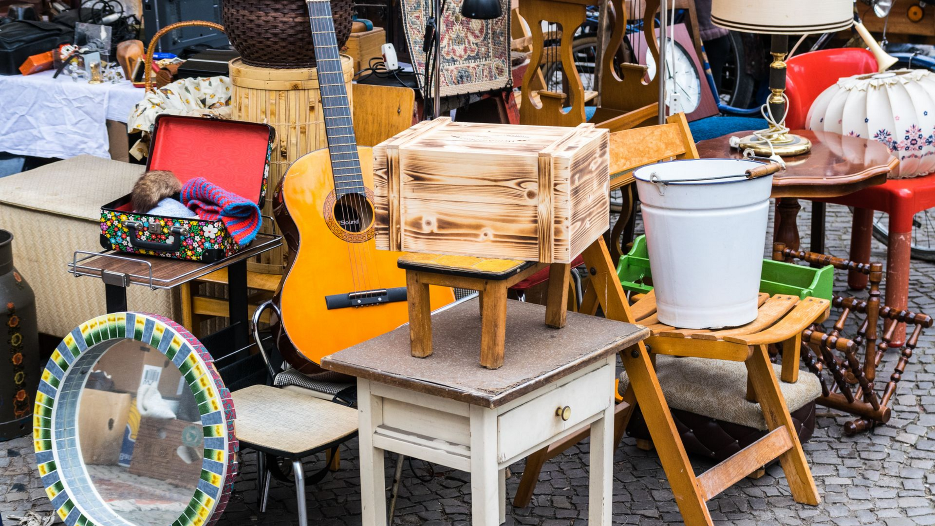 Scène de marché aux puces : divers objets d'occasion exposés sur des tables et empilés.