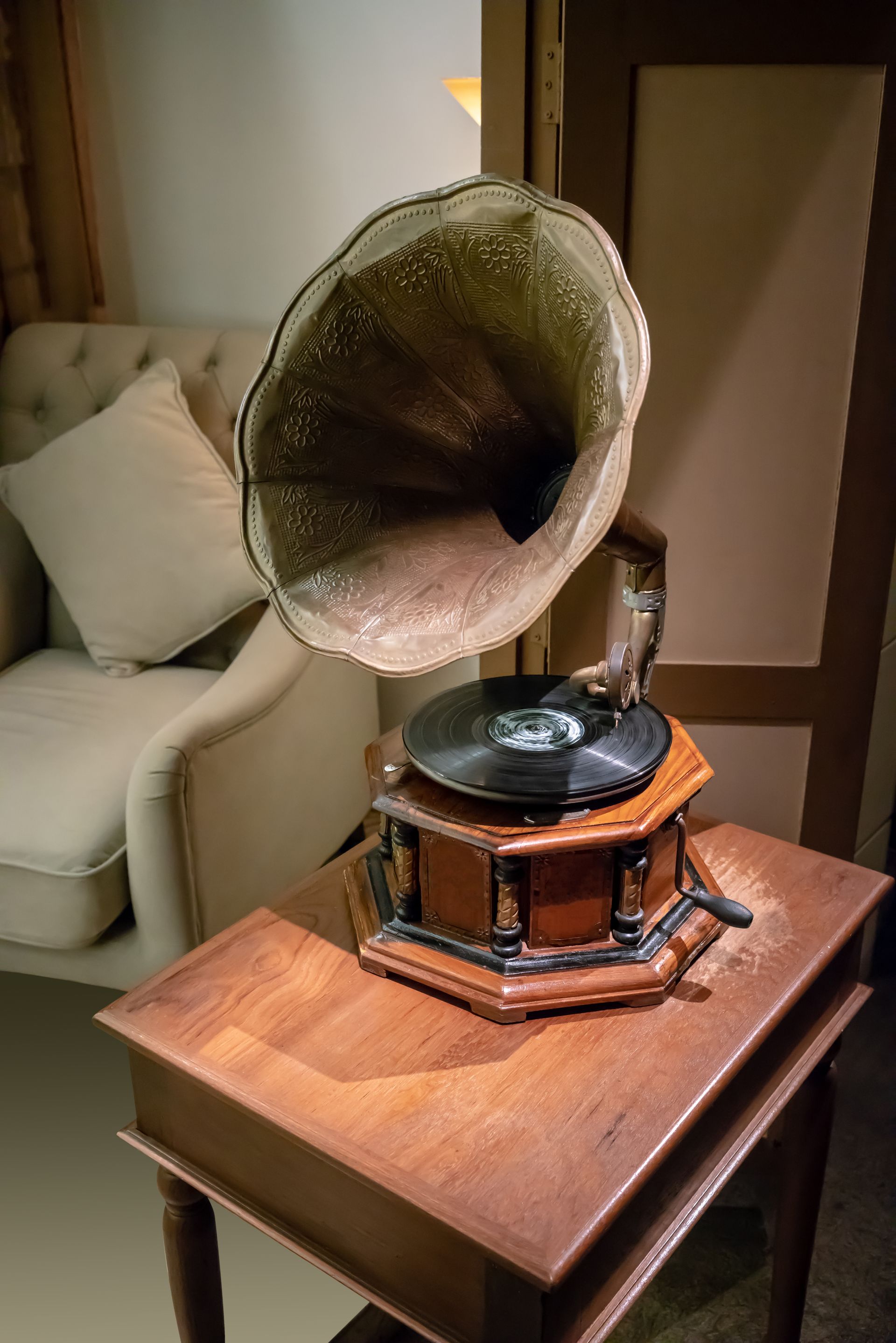 Gramophone ancien avec grand pavillon sur une table en bois, près d'un fauteuil rembourré.