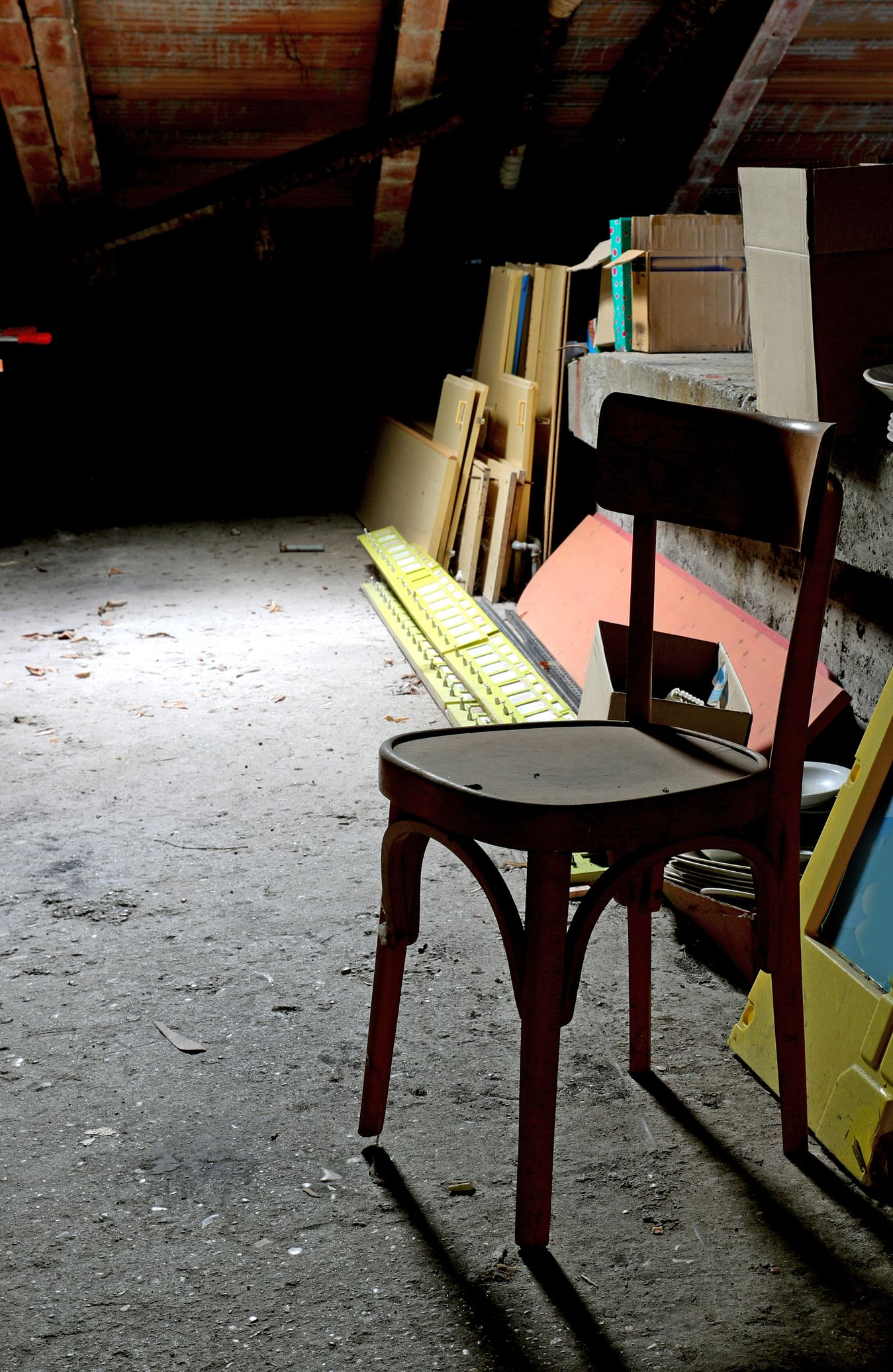 Une chaise patinée par les intempéries se trouve dans un grenier faiblement éclairé et poussiéreux avec divers objets.