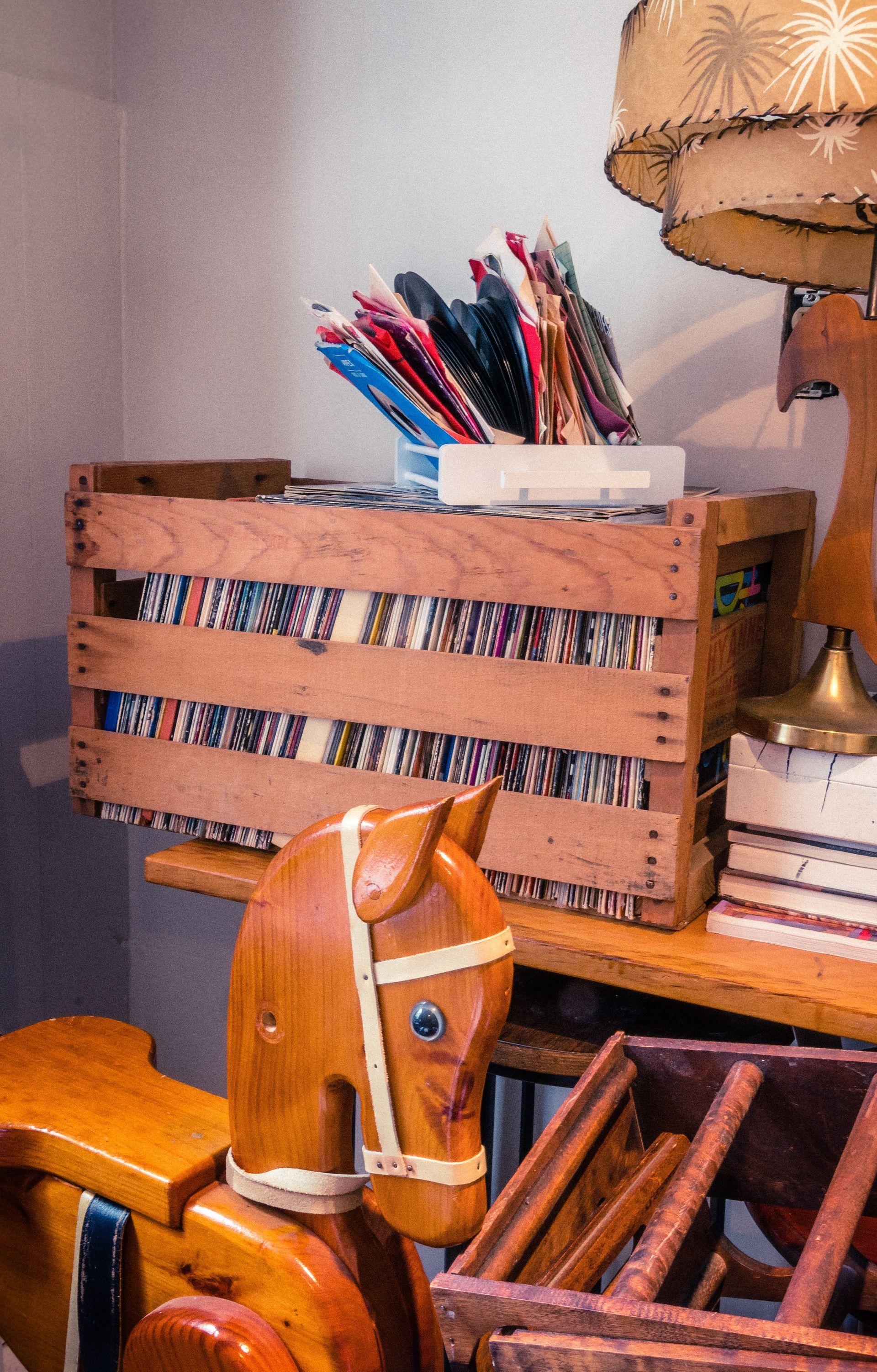 Cheval à bascule en bois à côté d'une caisse en bois remplie de tissu et de crayons, près d'une lampe.