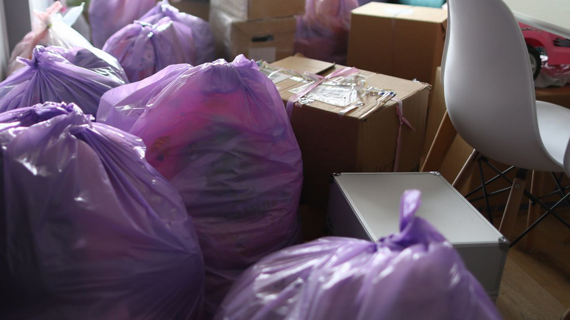 Sacs-poubelle violets et boîtes en carton dans une pièce, prêts à être déplacés ou éliminés.
