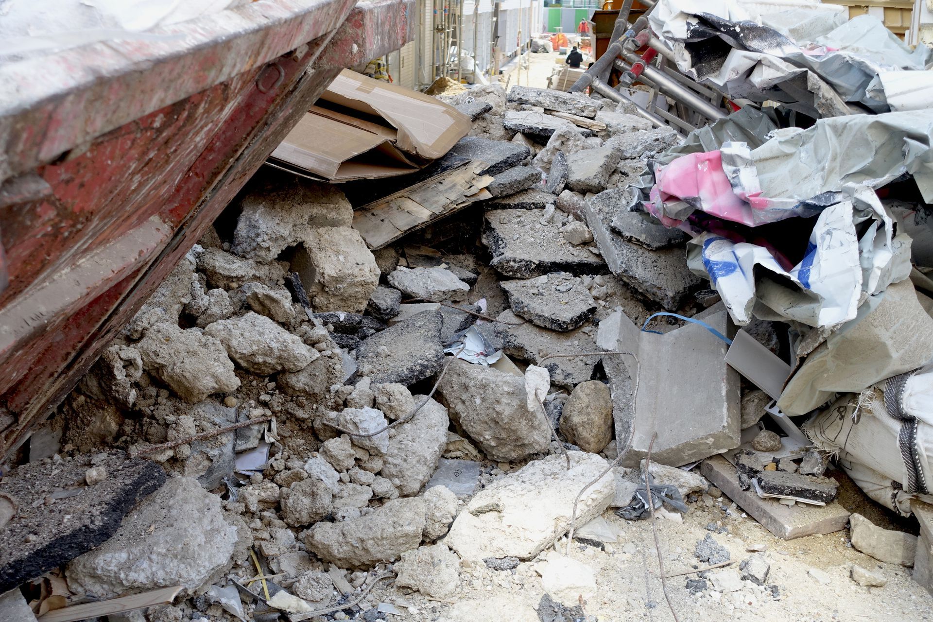 Tas de gravats et de débris, probablement des déchets de construction, à côté d'un conteneur rouge.