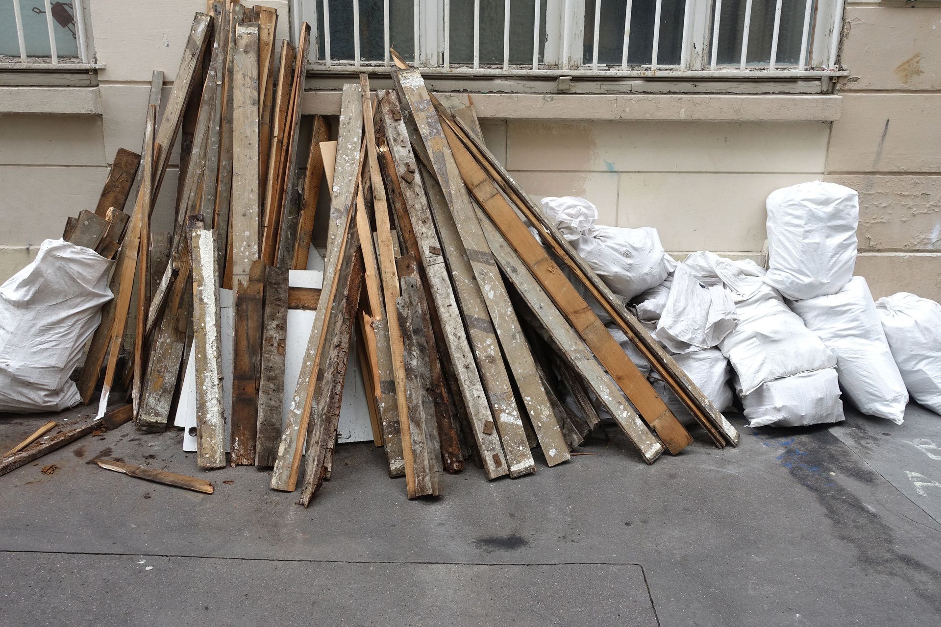 Pile de planches et de sacs blancs dans une rue de la ville devant un bâtiment.
