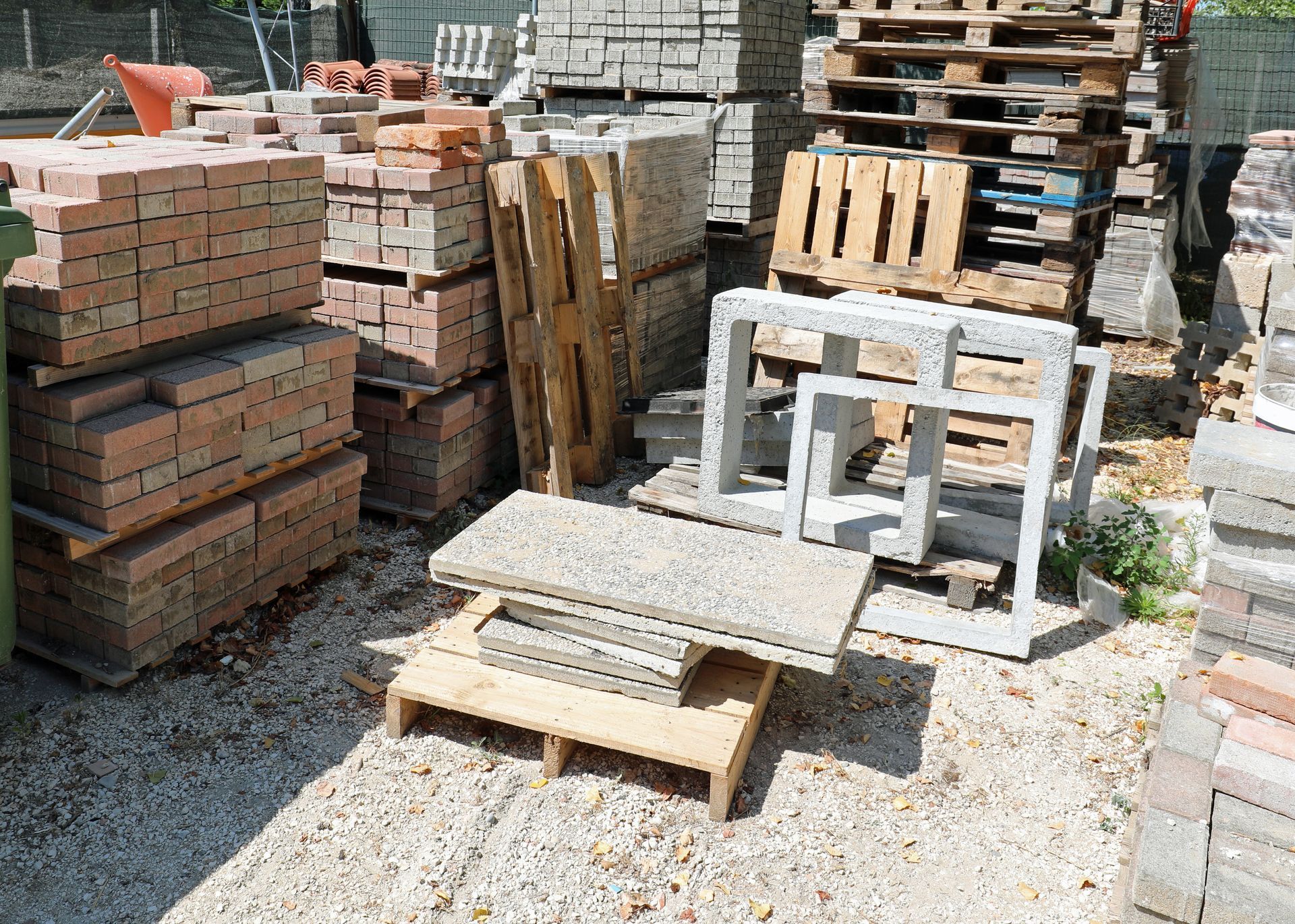 Des tas de briques et de blocs de pierre, ainsi que des palettes en bois, à l'extérieur sur une surface de gravier.