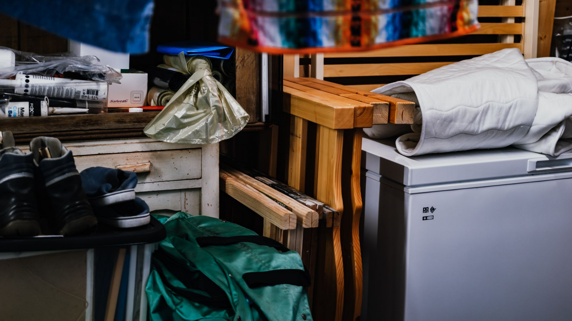 Espace de rangement encombré avec des chaussures, des structures en bois, un sac vert et un réfrigérateur.