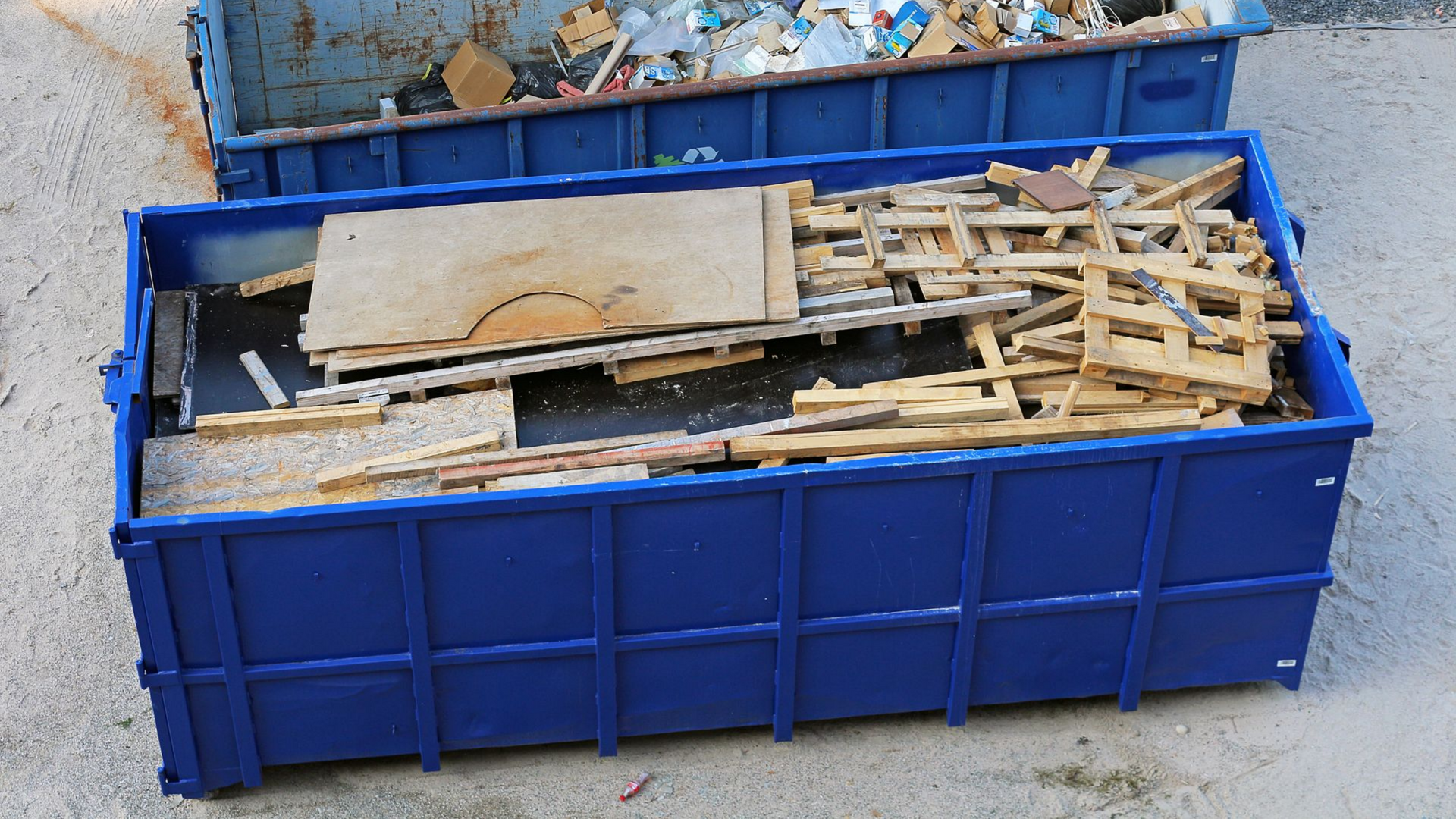 Deux bennes bleues remplies de débris de construction, à l'extérieur.