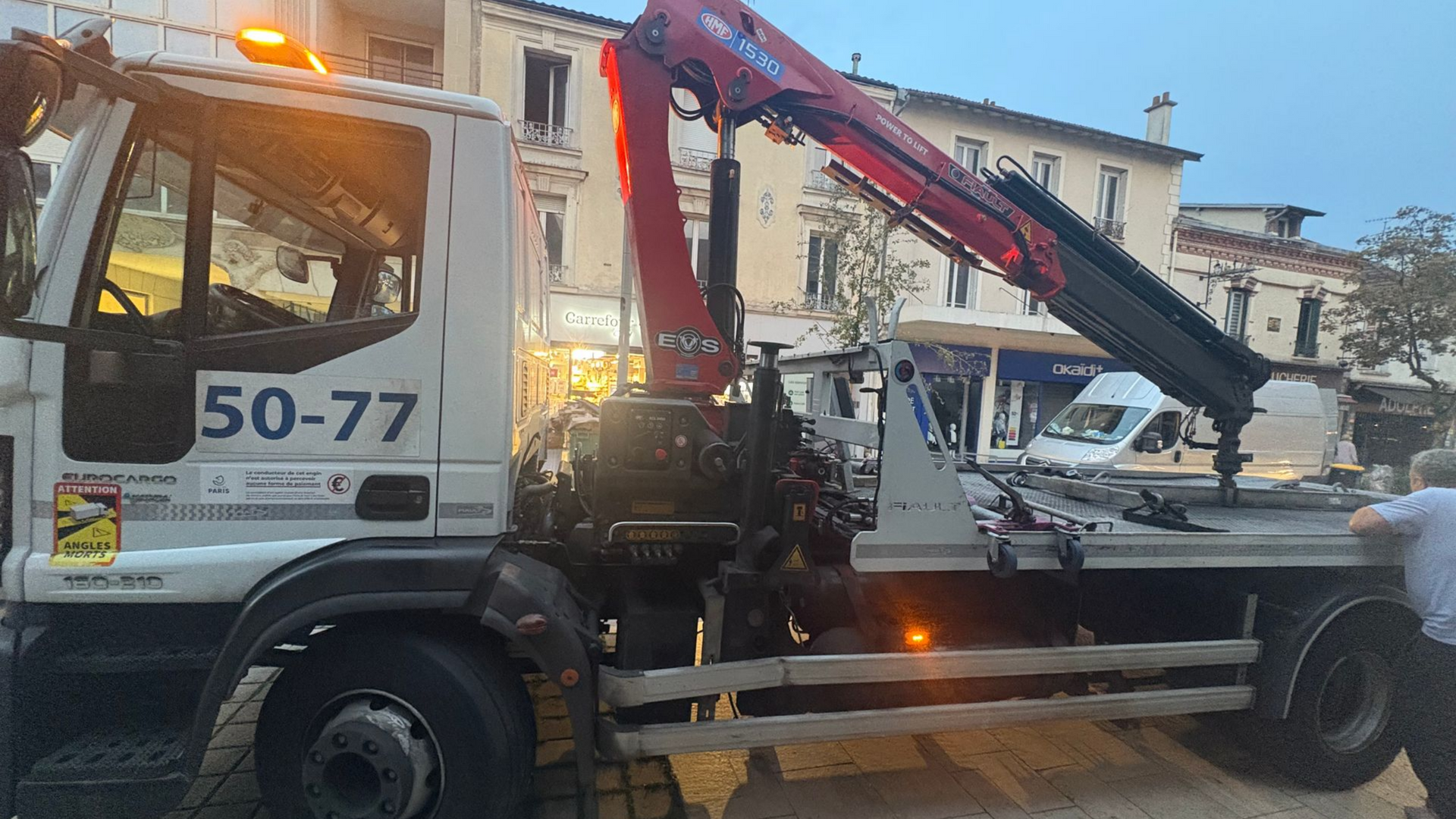 Dépanneuse avec grue sur la route, feux allumés.