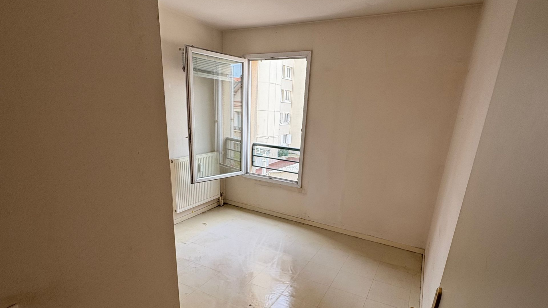 Pièce vide avec une fenêtre, des murs blancs et un radiateur.