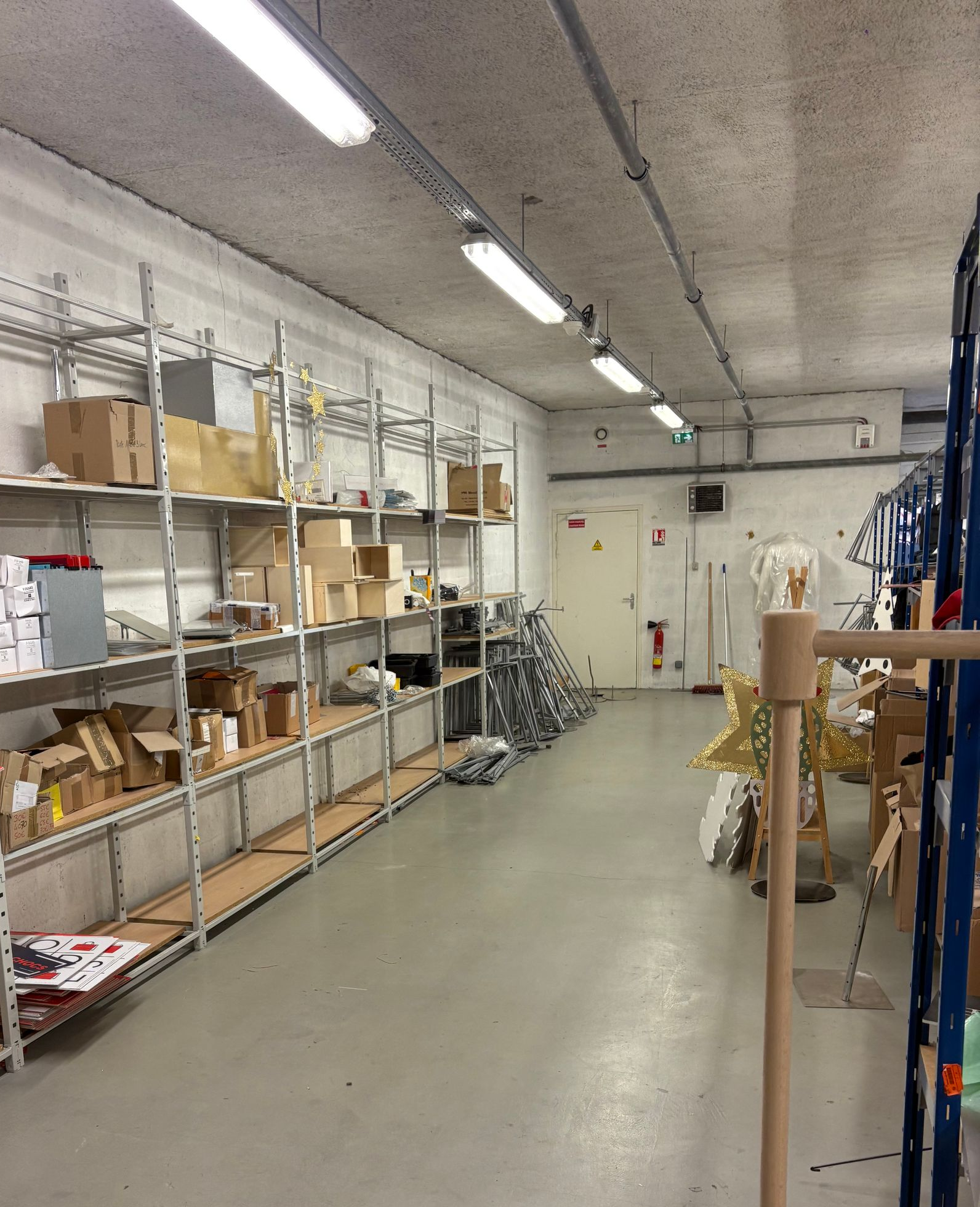 Intérieur d'entrepôt avec étagères métalliques remplies de boîtes et d'articles ; sol en béton, éclairage fluorescent.