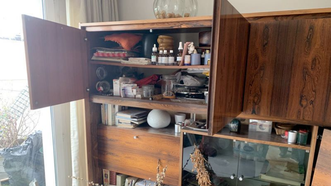 Armoire en bois avec porte ouverte révélant des étagères avec divers objets.