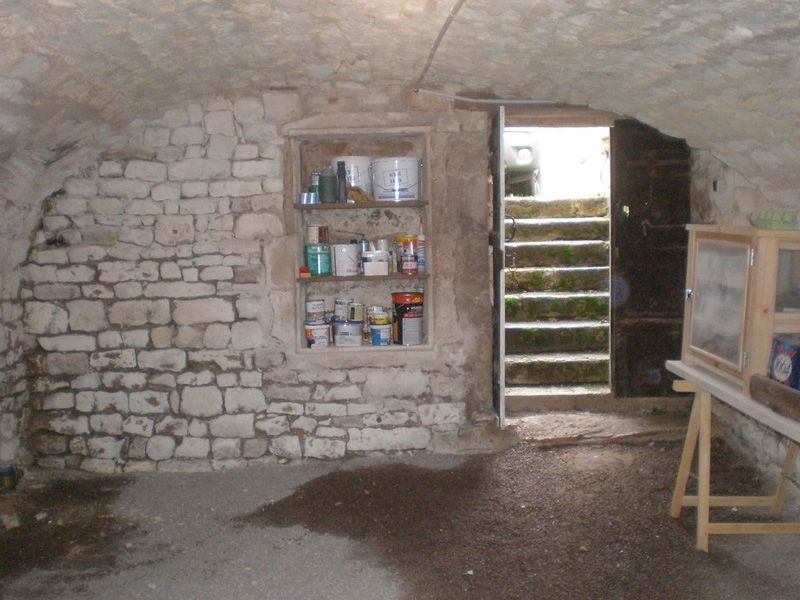 Cave aux murs de pierre avec porte ouverte donnant sur un escalier.