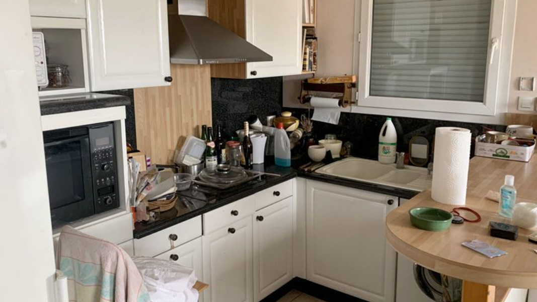 Petite cuisine avec armoires blanches, comptoirs noirs et une table ronde en bois.