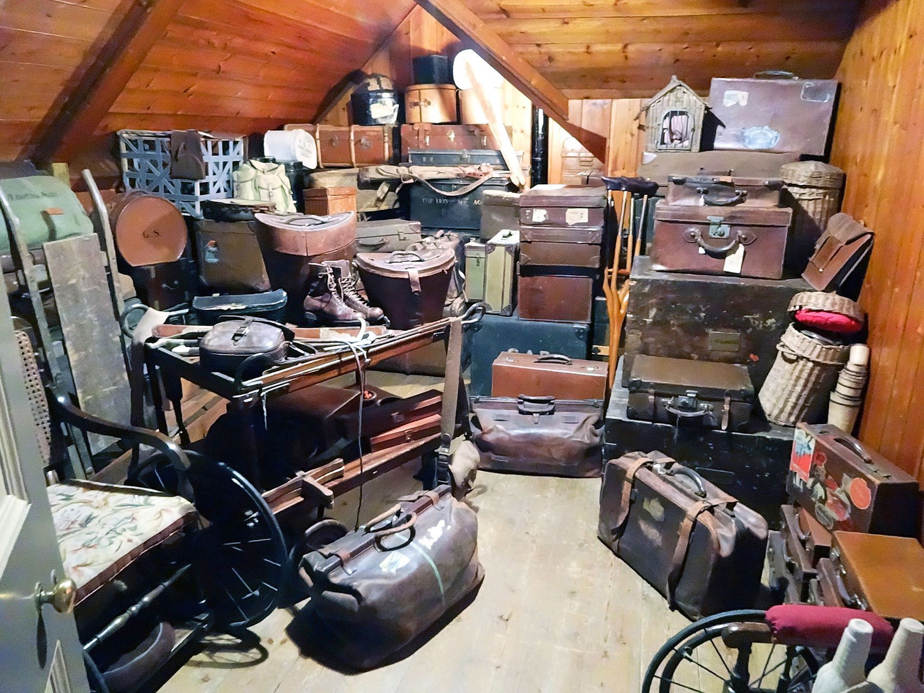 Grenier encombré rempli de vieux bagages, malles, cartons et objets divers. Murs et plafond en bois.