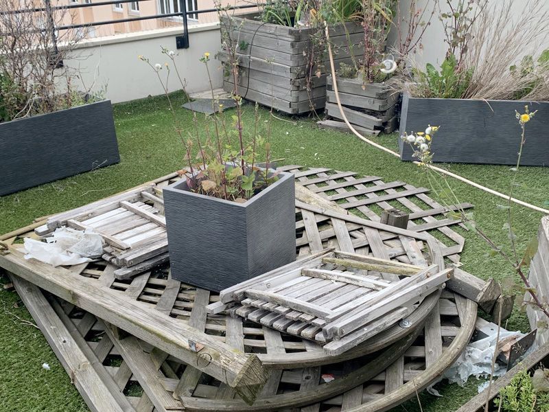 Mobilier de jardin en bois et pots de fleurs sur un toit en pelouse artificielle verte.