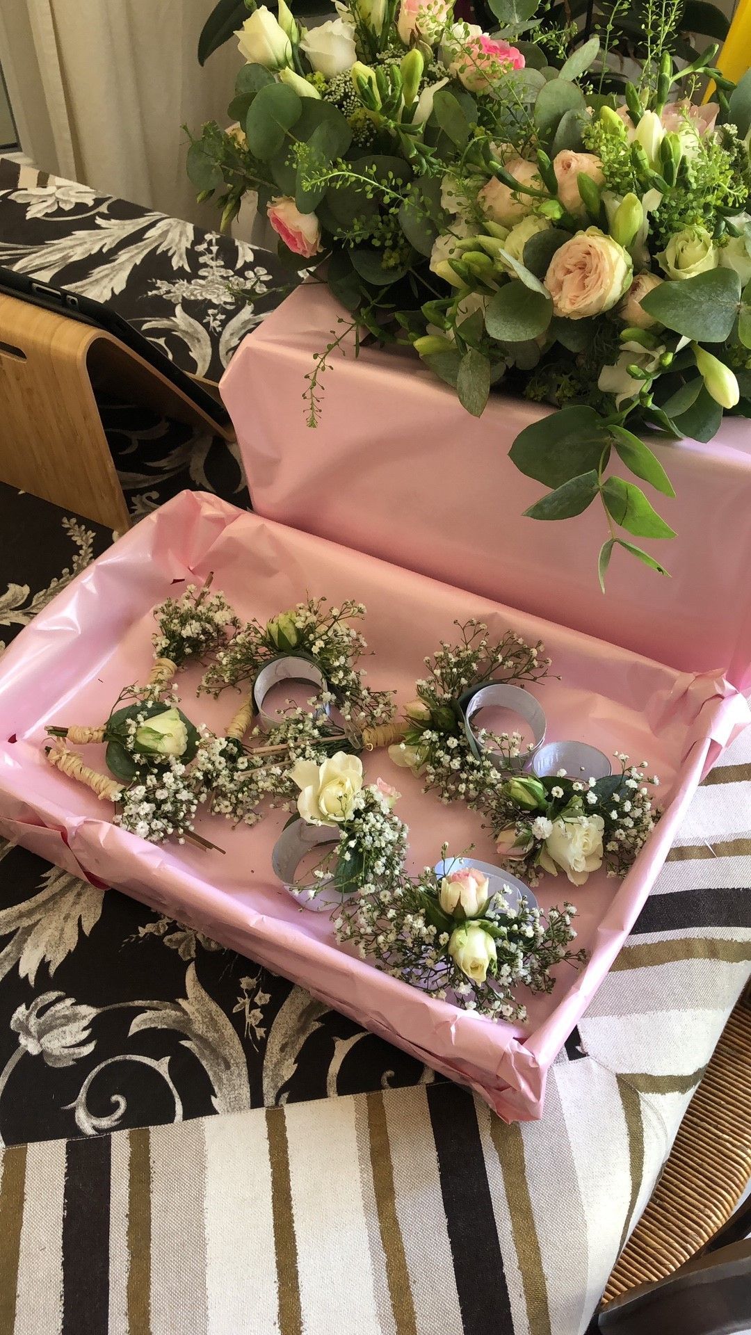 Bouquet de petits corsages dans une boîte rose, à côté d'une composition florale plus importante.