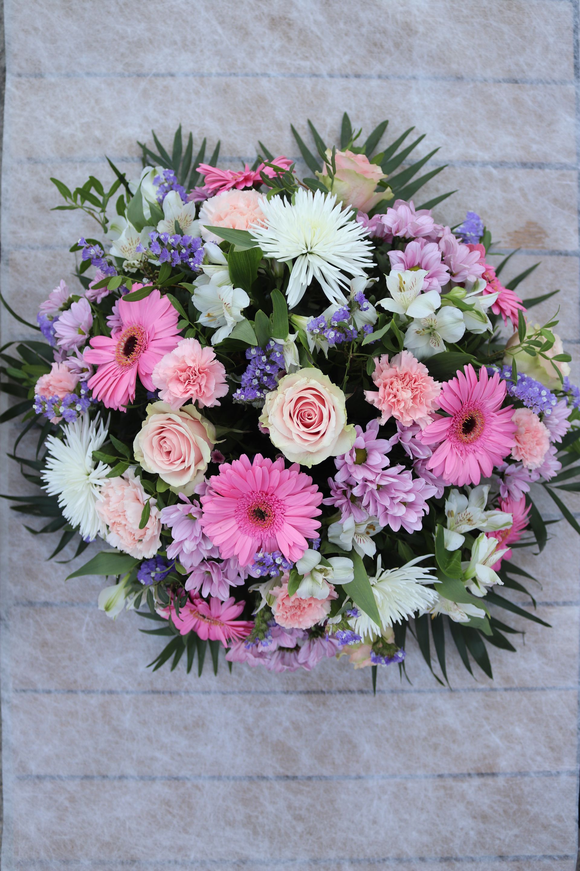 Un arrangement circulaire de fleurs roses, blanches et violettes avec de la verdure sur une surface texturée.
