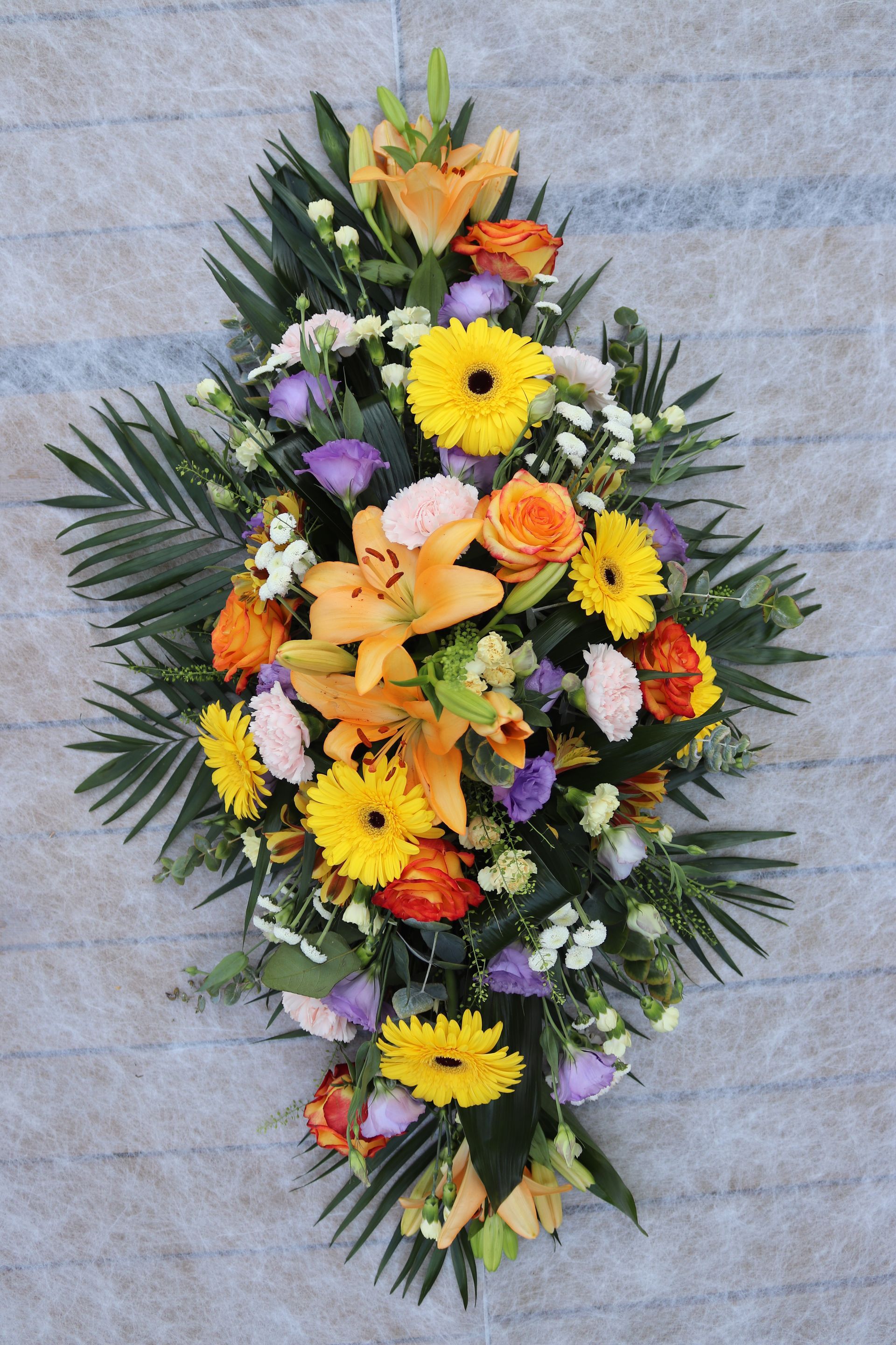 Composition florale avec des fleurs jaunes, oranges et violettes et du feuillage vert.