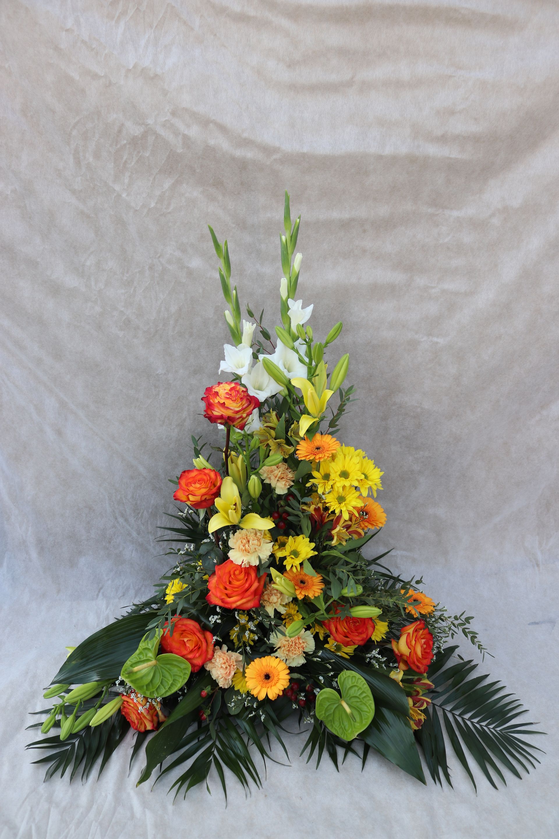 Composition florale de fleurs orange, jaunes et blanches avec du feuillage vert sur un fond texturé.