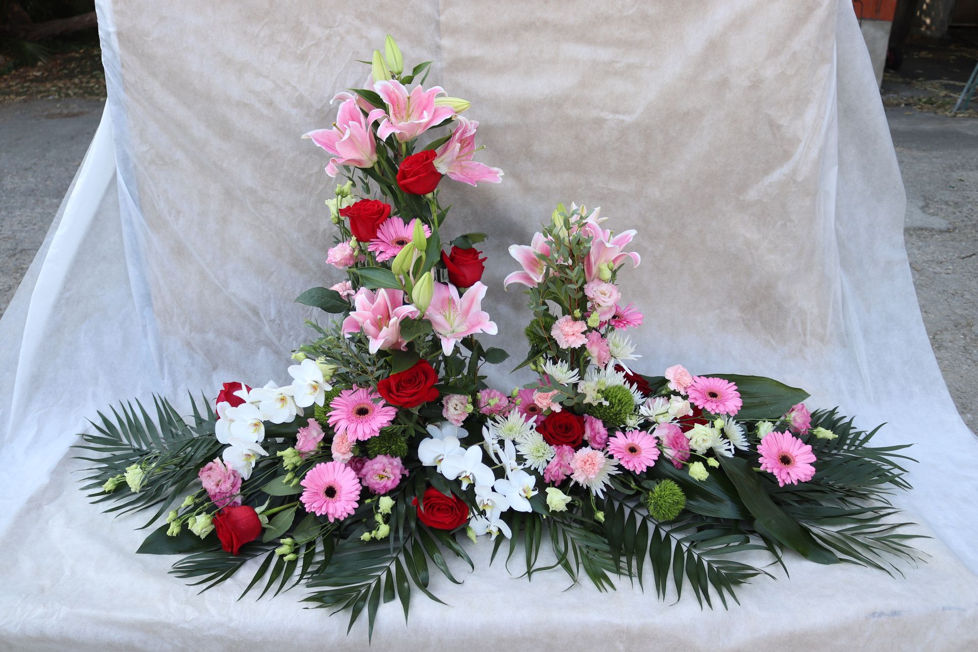 Composition florale avec des lys roses, des roses rouges et du feuillage vert.