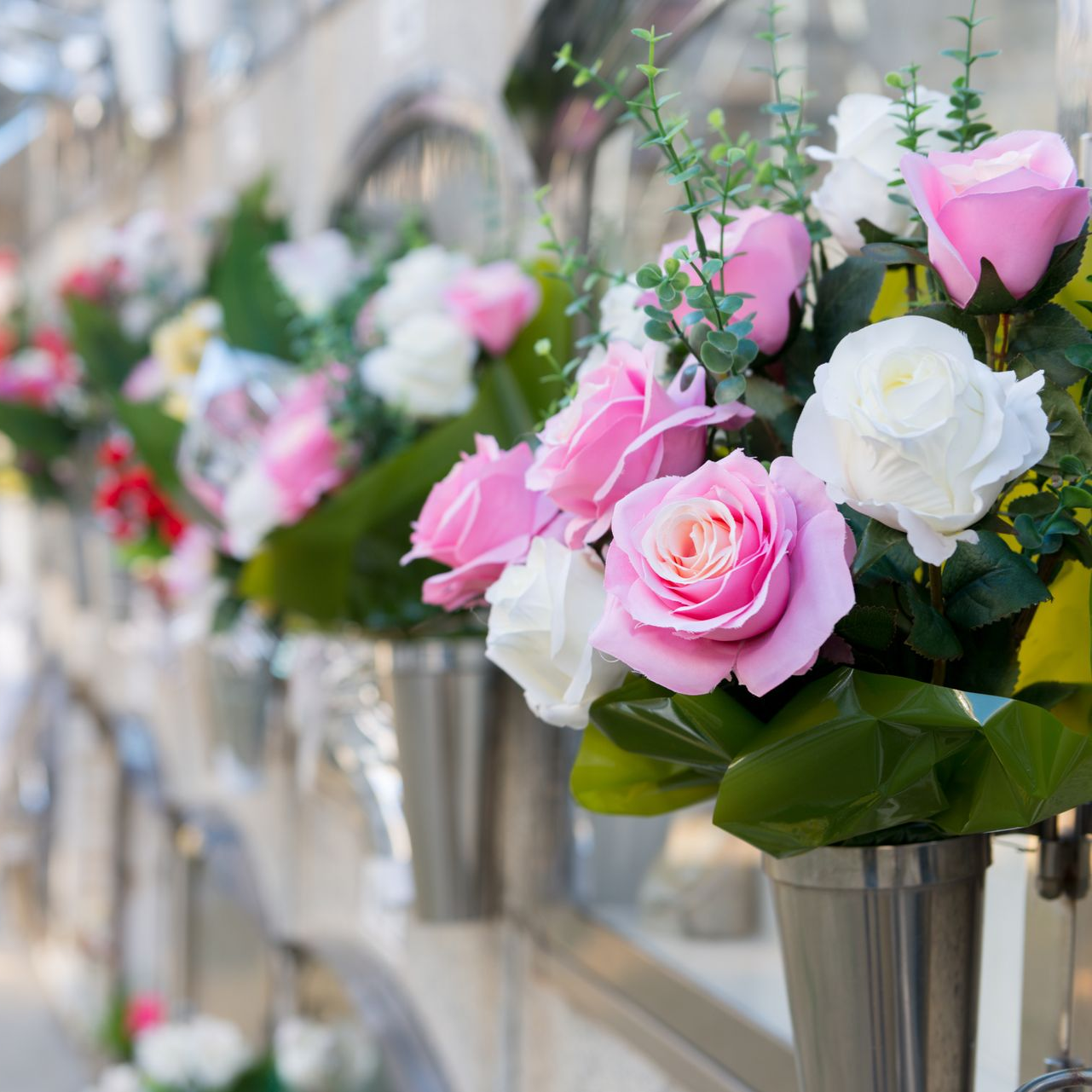 Bouquets de roses, rose et blanc dans des vases en métal, dans un cimetière.