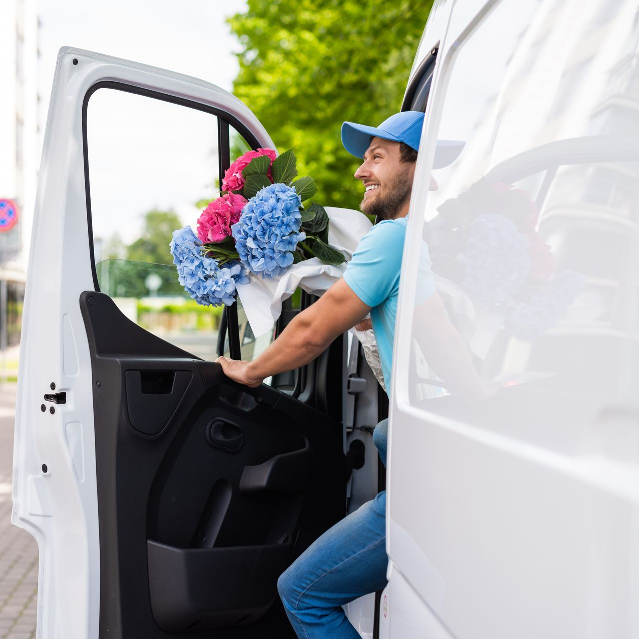 Un livreur de fleurs sort d'une camionnette blanche avec un bouquet d'hortensias rose et bleu.