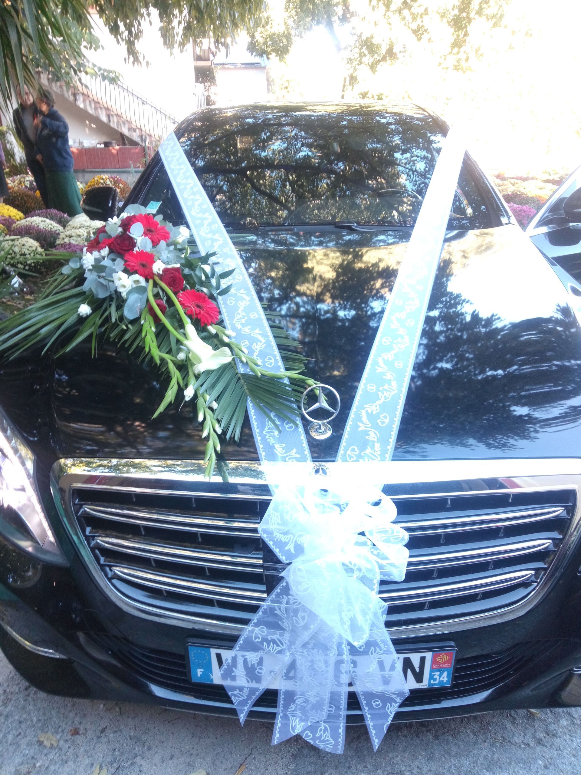 Voiture noire décorée de fleurs rouges et blanches et d'un nœud blanc, probablement pour un mariage.