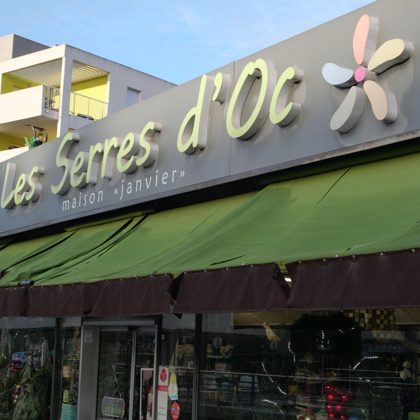 Enseigne de la boutique Les Serres d'Oc, avec un auvent vert et un logo floral.