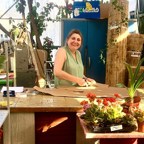 Femme souriante, découpant du carton sur une table de rempotage dans une serre avec des plantes.
