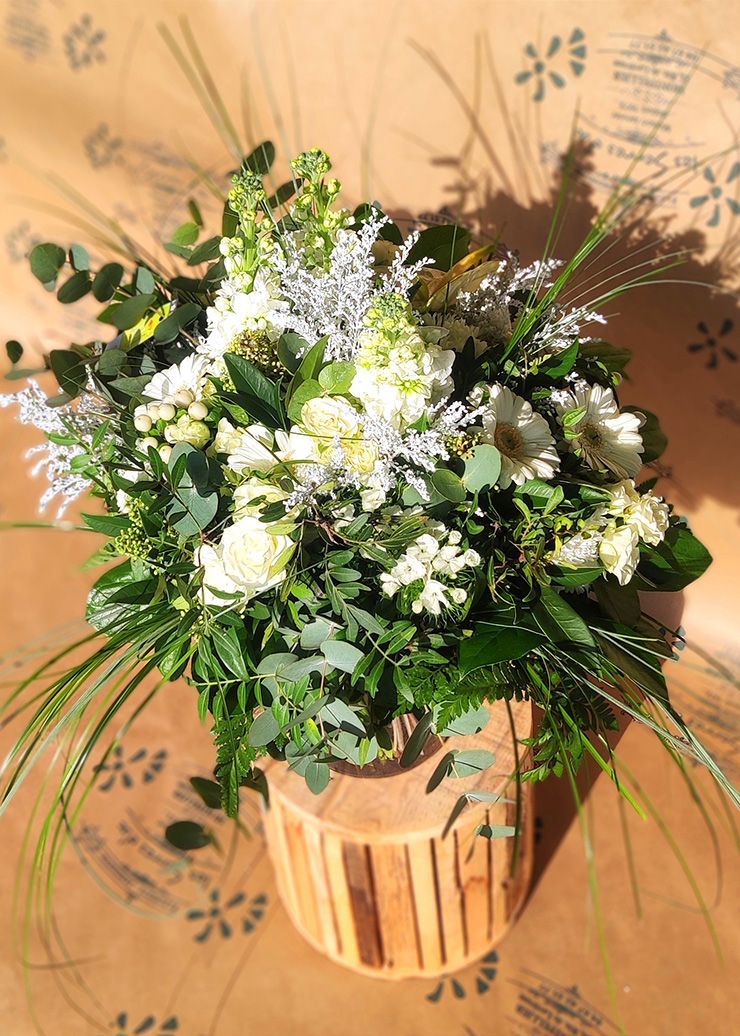 Bouquets de fleurs blanc et vert dans un vase en bois, posés sur une surface à motifs.