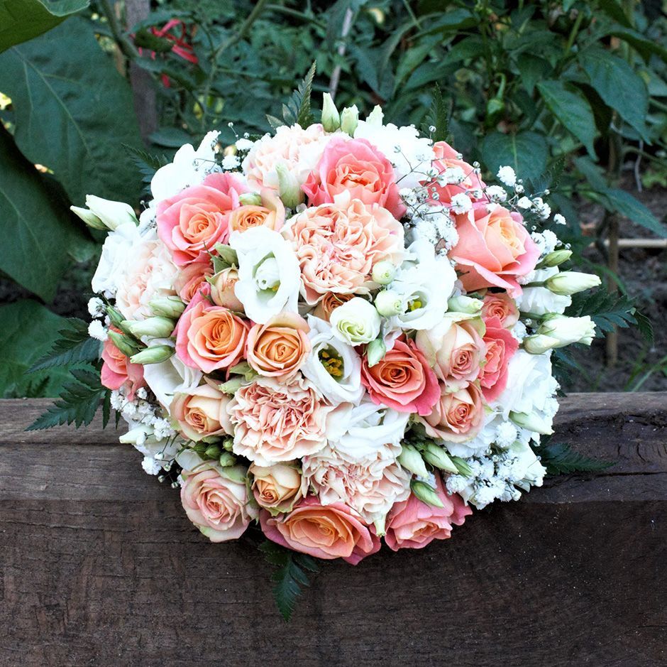 Bouquet de roses, pêche et roses, d'œillets et de fleurs blanches sur une surface en bois.