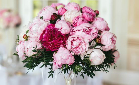 Bouquet de pivoines roses et rose foncé dans un vase en verre, posé sur une nappe blanche, fond flou.