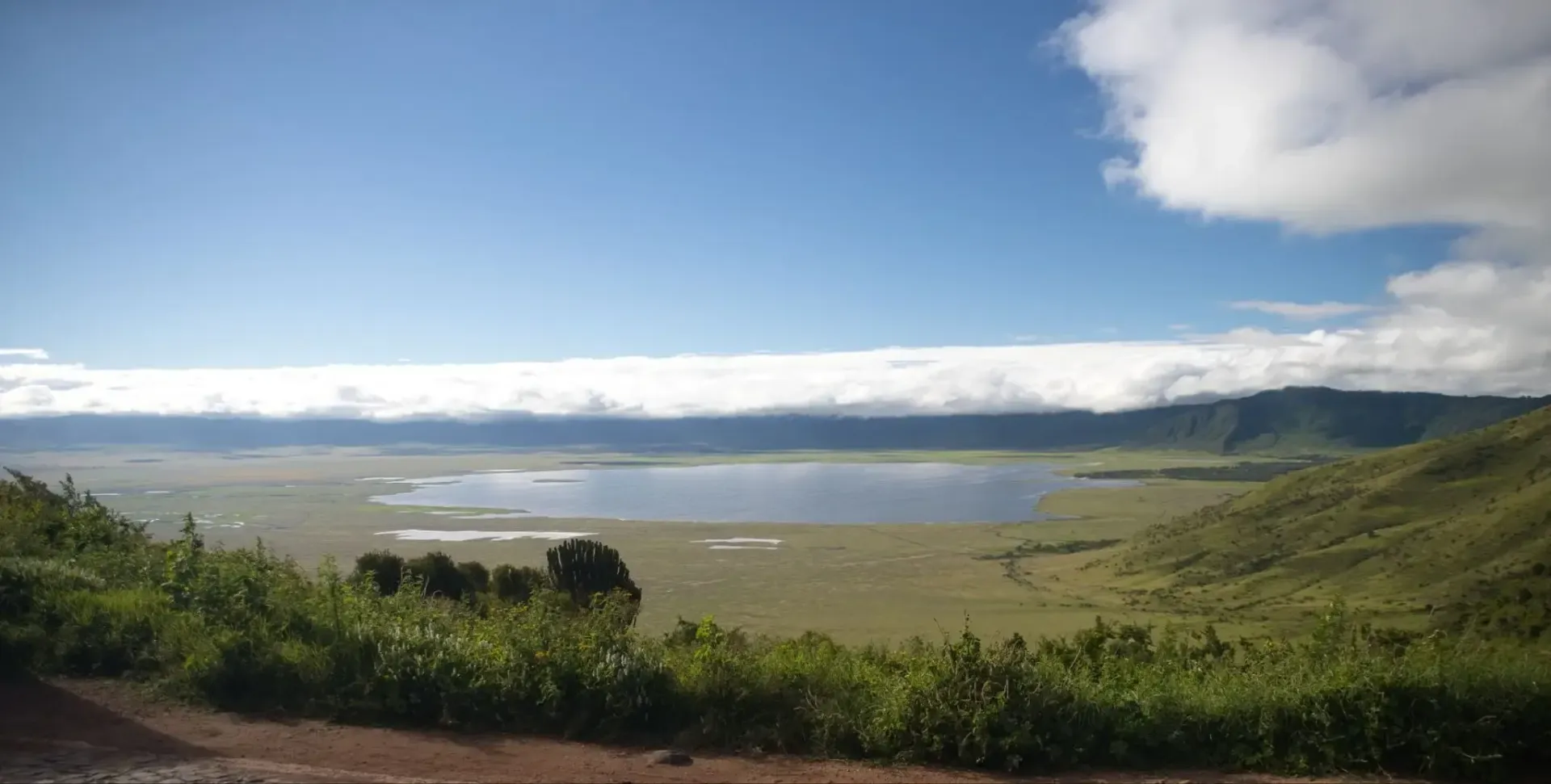 Amplia laguna costera de aguas tranquilas, colinas verdes y un cielo azul brillante con nubes.