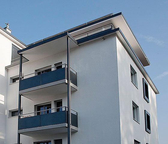 Ein weißes Gebäude mit blauen Balkonen vor einem blauen Himmel