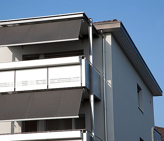 Ein weißes Gebäude mit schwarzen Markisen auf den Balkonen