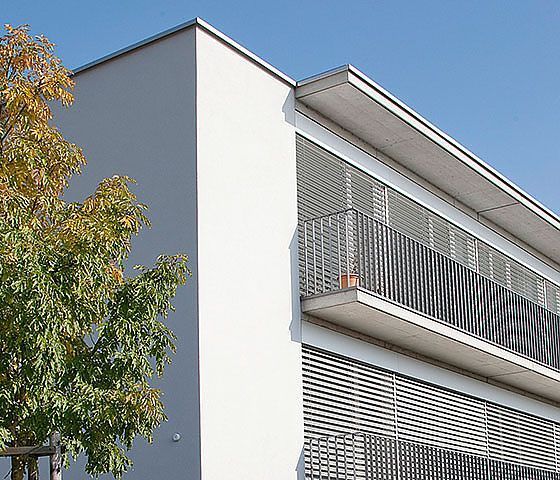 Ein weißes Gebäude mit einem Balkon und einem Baum davor