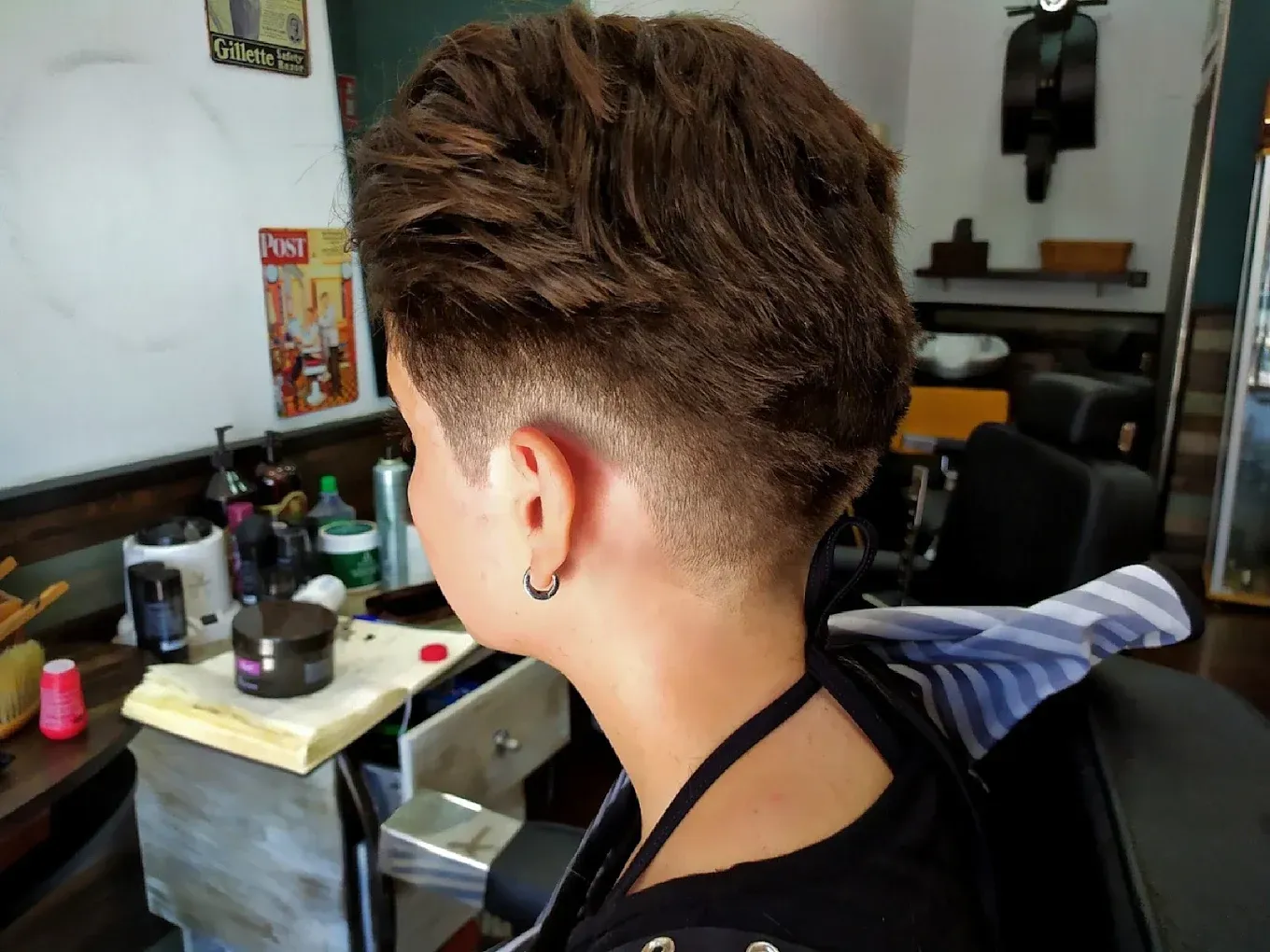 Persona con corte de pelo rapado en una barbería, vista de perfil. Cabello corto recogido y recogido.