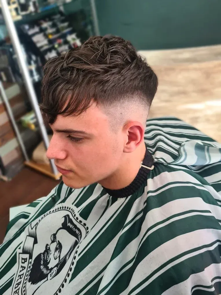 Hombre con un corte de pelo descolorido en una barbería, con una capa a rayas. Su cabello está peinado con volumen.