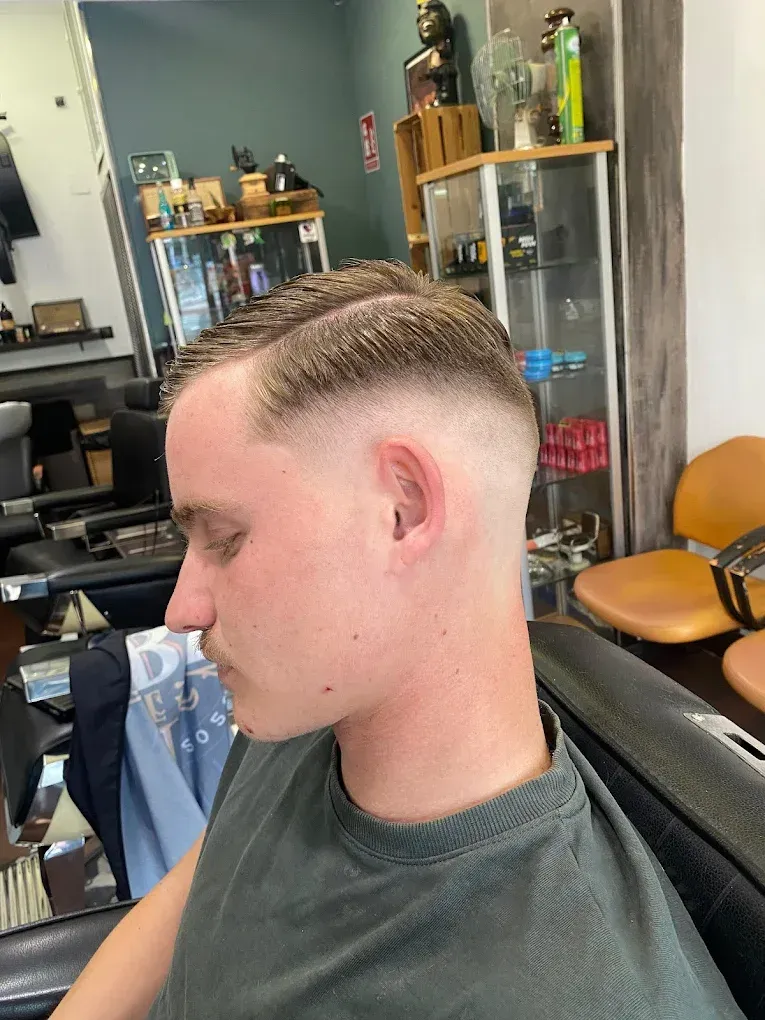 Hombre con corte de pelo descolorido, con raya a un lado, en una barbería.
