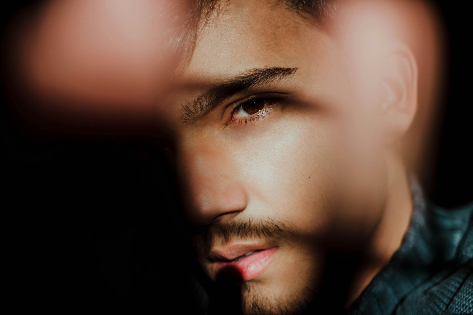 Primer plano del rostro de una persona con sombra. Tiene cabello oscuro, perilla y expresión seria.