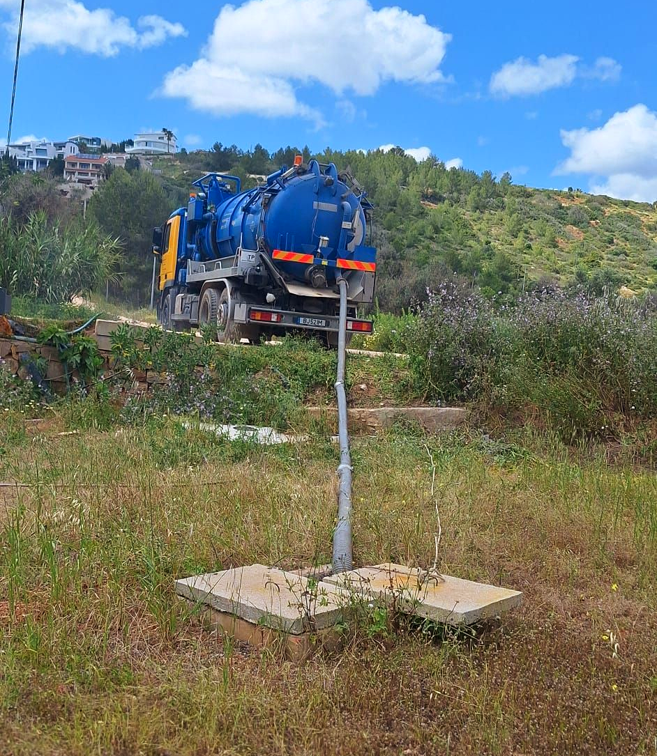 Um operário com capacete e máscara respiratória entra em um bueiro com mangueiras e correntes ao redor da abertura.