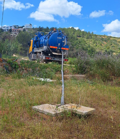 Desentupimentos Um operário com capacete e máscara respiratória entra em um bueiro com mangueiras e correntes ao redor da abertura.