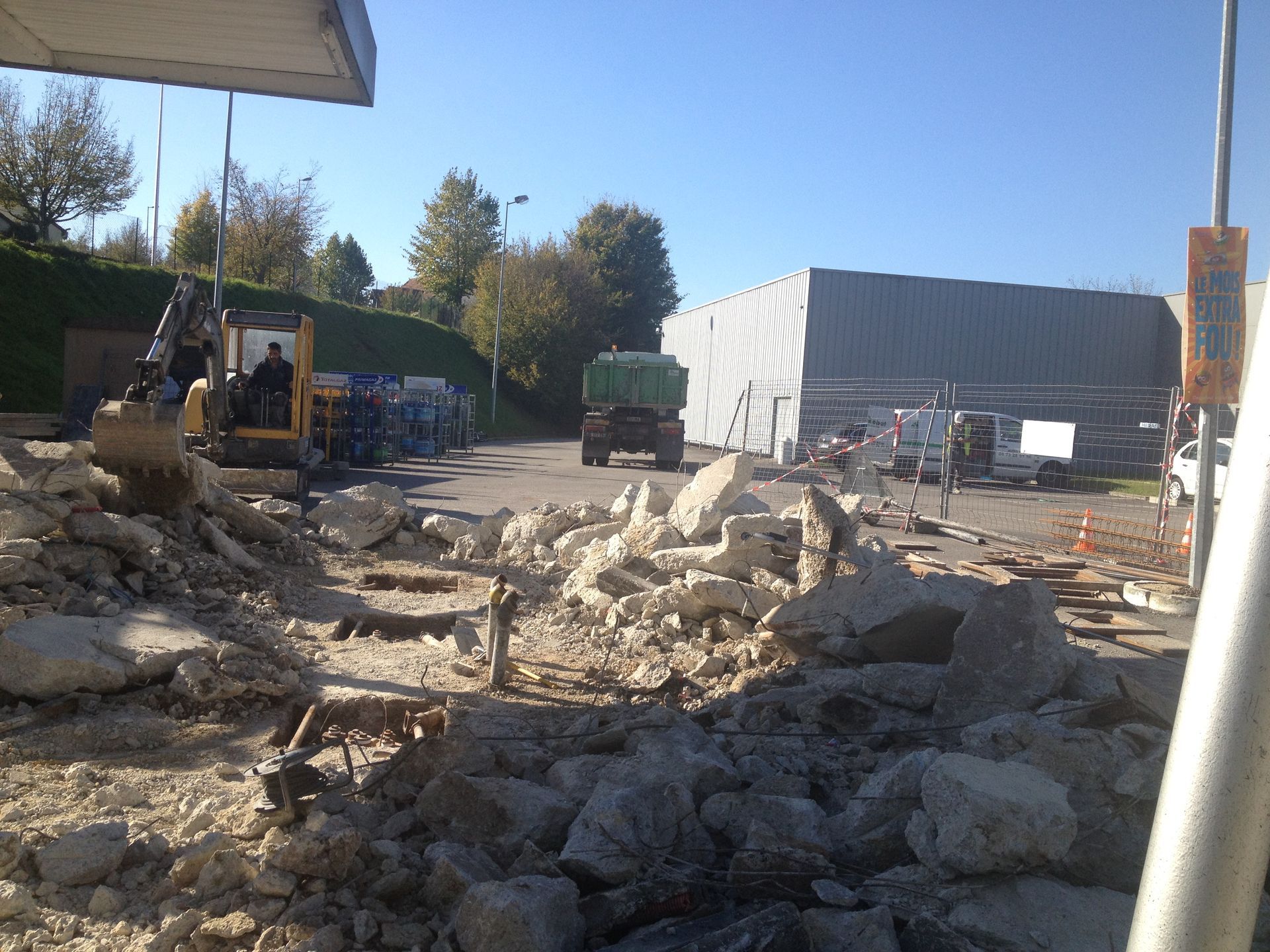 Une excavatrice dégage des débris de béton sur un chantier de construction, avec un grand bâtiment