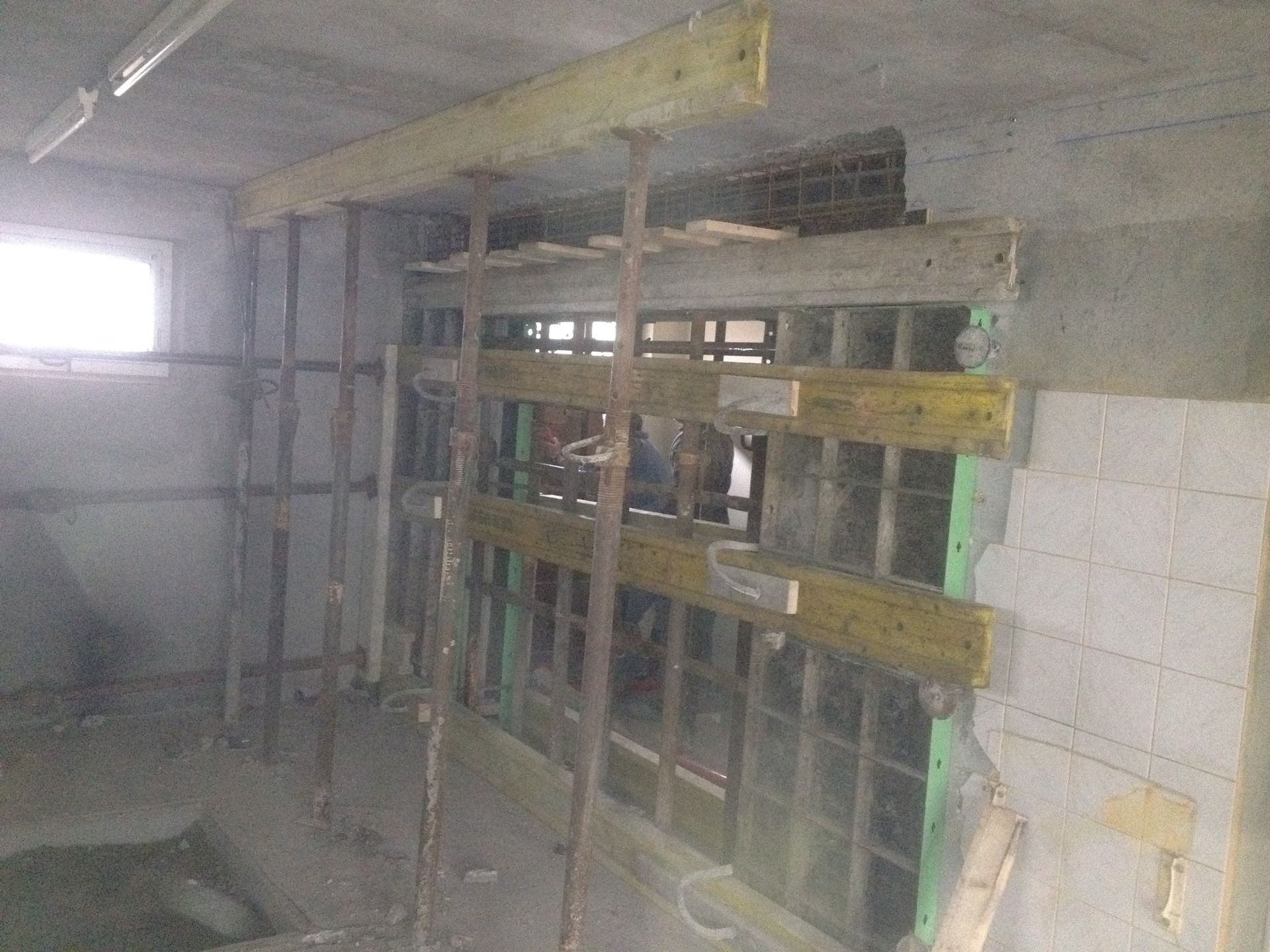 Intérieur d'un chantier de construction, supports en béton et en bois, un mur partiel avec des ouvertures.